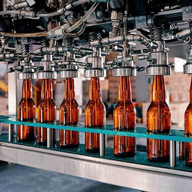 Szklane butelki przemieszczają się przez zakład produkcji napojów. Monitorowanie twardości wody ma duże znaczenie dla zarządzania jakością produktu.